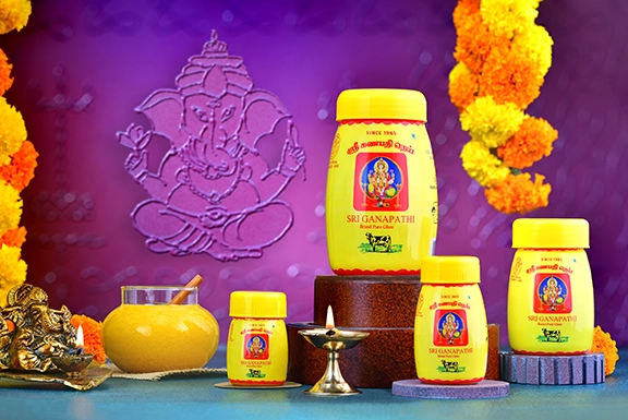 Sri Ganapathi ghee jars placed by a traditional brass diya lamp and a carved Lord Ganesha background.